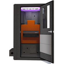 Load image into Gallery viewer, Front view of WhisperRoom&#39;s Voice Over Basic Package - a 4&#39; x 4&#39; single-wall vocal booth, thoughtfully equipped with acoustic treatment, a functional desk, studio lighting, and a variety of premium features. The right-hinged door is open, revealing the interior adorned with vibrant orange StudioFoam, creating an inviting recording space.

