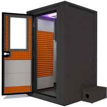 Load image into Gallery viewer, Side view of the WhisperRoom&#39;s Voice Over Deluxe Package - a 4&#39; x 4&#39; double-wall vocal booth, thoughtfully equipped with acoustic treatment, a functional desk, studio lighting, and an array of premium features. The left-hinged door is open, revealing the interior enhanced by vibrant orange StudioFoam, creating an ideal recording atmosphere.
