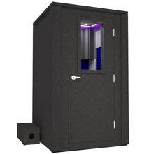 Load image into Gallery viewer, Angled view of the WhisperRoom&#39;s Voice Over Deluxe Package - a 4&#39; x 4&#39; double-wall vocal booth, meticulously designed with acoustic treatment, a functional desk, studio lighting, and a comprehensive range of premium features. The right-hinged door is closed, and the interior is accentuated with vibrant blue StudioFoam, creating an ideal recording environment.
