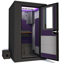 Load image into Gallery viewer, Angled view of WhisperRoom&#39;s Voice Over Deluxe Package - a 4&#39; x 4&#39; double-wall vocal booth, meticulously designed with acoustic treatment, a functional desk, studio lighting, and a comprehensive range of premium features. The right-hinged door is open, revealing the interior enhanced by elegant purple StudioFoam, creating an ideal recording atmosphere.

