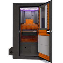 Load image into Gallery viewer, Frontal view of the WhisperRoom&#39;s Voice Over Deluxe Package - a 4&#39; x 4&#39; double-wall vocal booth, thoughtfully equipped with acoustic treatment, a functional desk, studio lighting, and a comprehensive range of premium features. The right-hinged door is open, revealing the interior enhanced by vibrant orange StudioFoam, creating an ideal recording atmosphere.
